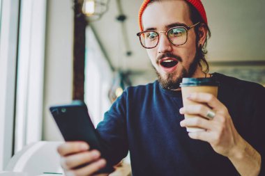 Şaşırmış hipster adam cep telefonundan şok edici içerik haberleri izliyor ve merak ediyor. Şaşırmış erkek blogcu bir mesaj aldı. Millennial 'dan bir adam, alışveriş promosyonları için arıyor.