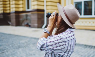 Beyaz kadın turist, şehirde eski moda kameralarla gezinirken şehir merkezinin fotoğraflarını çekiyor. Moda şapkalı genç hippi kız, boş zamanlarında fotoğraf çekiyor.
