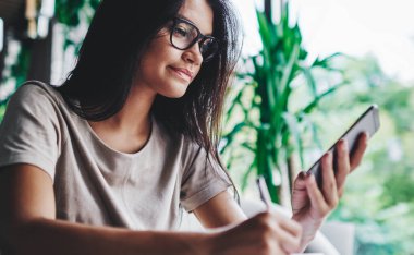 Milenyum Kafkasyalı kadın sosyal ağlardan haber okuyor kafede cep telefonu kullanıyor, kadın blogcu akıllı telefon üzerinde online araştırma yapıyor ve not defterinde paylaşım için yazı yazıyor.