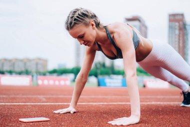 Spor giyim sektöründe aktif ve sportif bir bayan arka planda kırmızı piste, akıllı telefon ve bir şişe su itiyor.