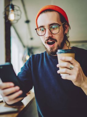 Şaşırmış hipster adam cep telefonundan şok edici içerik haberleri izliyor ve merak ediyor. Şaşırmış erkek blogcu bir mesaj aldı. Millennial 'dan bir adam, alışveriş promosyonları için arıyor.