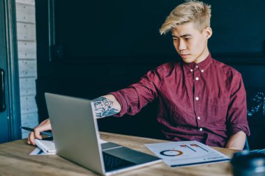 Modern uzayda kablosuz internet kullanarak modern dizüstü bilgisayarda webinar çalışmasını izleyen düşünceli Çinli hippi öğrenci. Netbook Cihazı 'nda serbest çalışan Milenyum Asyalı genç adam.