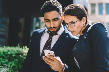 Katı siyah takım elbiseli, konsantre olmuş çok ırklı iş arkadaşları yazın şehir merkezinde cep telefonlarında birbirleriyle sohbet ediyorlar.