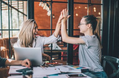Neşeli bayan iş arkadaşlarıyla aynı masada oturup beşlik çakan ve takım halinde gülen adamın yan görüntüsü.