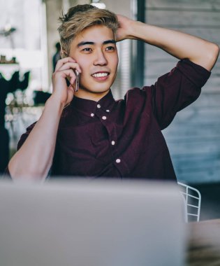 Başarılı genç Asyalı iş adamı, modern uzayda dizüstü bilgisayarın uzaktan kumandası sırasında operatörle birlikte akıllı telefondan arıyor. Çinli hippi adam cep telefonuyla eğleniyor.