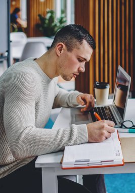 Gündelik giysiler giyen iki yetenekli öğrenci, modern ofiste kablosuz internet bağlantısı kullanarak dizüstü bilgisayarların başında sınavlara hazırlanıyor. 