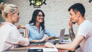 Gündelik giysiler içinde bir grup genç, kafeteryada masaların üzerinde aletlerle oturuyor ve ortak bir proje geliştirmek için işbirliği yapıyorlar.
