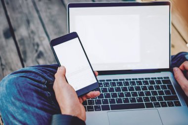 Bin yıllık adamın interneti taramak için cep telefonuyla cep telefonu bağlantısını kullanarak uzaktan bilgisayarla çalışırken çekilmiş görüntüsü. Akıllı telefon ve netbook cihazları olan yetenekli bir erkek.