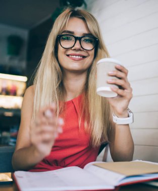 Aşağıdan, gözlüklü genç bir kız öğrenciden. Kameraya bakıyor, elinde içecek, not alıyor ve kafede oturuyor.