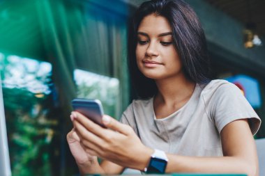 Sosyal ağlarda yeni beslemeleri kontrol eden genç hippi kız boş zamanlarında kafede netbook 'la oturuyor, olumlu milenyum kadını internetteki uzak iş için kablosuz bağlantıyı kullanarak multimedya dosyalarını paylaşıyor