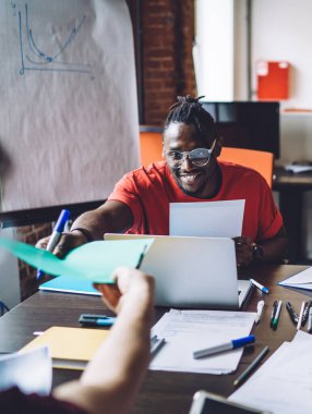 Modern ofiste masa başında oturup gülerek yeni projeleri tartışan mutlu, çok ırklı genç insanlar.