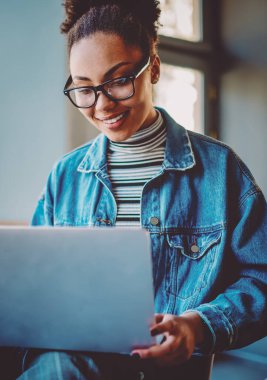 Pozitif esmer tenli kız öğrenci boş zamanlarında online alışveriş yapıyor, optik gözlüklü mutlu genç internet sitelerinde popüler internet sitelerinde komik videolar izliyor.