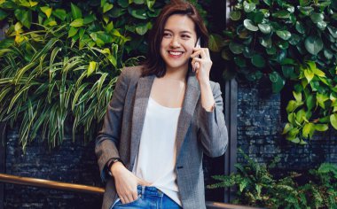 Mutlu, genç, gülümseyen, şık kıyafetler içinde, gri ceketli, mavi kotlu, telefonda konuşan güzel Asyalı kadın.