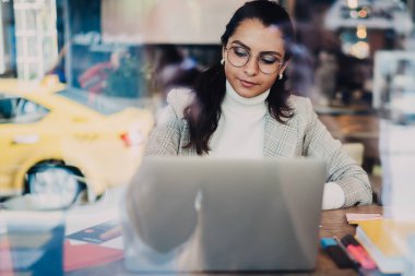 Gözlüklü ve gündelik giysiler içindeki muhteşem bir kadın, kafeteryadaki masada oturarak yeni bir başlangıç yaratıyor.