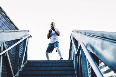 Tişörtlü, siyah eldivenli, kel, Afro-Amerikan bir boksörden şehrin açık gökyüzüne karşı gölgelerde boks maçı.