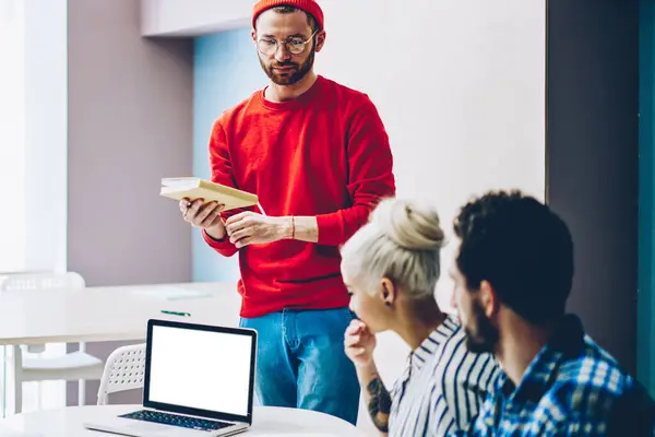 Young caucasian hipster guy speaking about his report share information with group of colleagues on lesson, creative leader of working crew having conversation with employees during meeting table