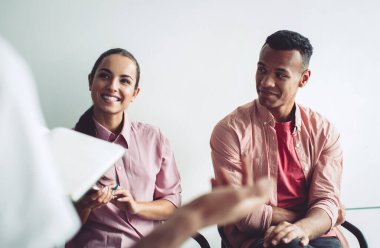 Sıradan giyinmiş neşeli beyaz kadın iş arkadaşından gelen bilginin sunumu sırasında gülümsüyor, kapalı alanda işbirliği yapan mutlu çok kültürlü insanlar, girişimcilik kavramı.