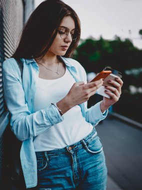 Sokak ortasında 4G internet bağlantısı kullanarak sosyal ağlarda sohbet etmek için kahve ile şık giyimli hippi kız. Şehir ortamında cep telefonu profilini güncelleyen genç bir kadın.