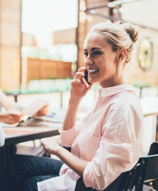 Neşeli yetişkin girişimci, açık modern açık uzay ofisindeki iş arkadaşlarıyla toplantı sırasında masasında otururken ve gözlerini kaçırırken telefonla konuşuyor.
