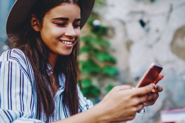 Kafe 'de boş zamanlarında cep telefonuyla mesaj gönderen neşeli, beyaz tenli esmer kadın, cep telefonuyla çalışan takipçilerden gelen geri bildirimlerle tatmin olan başarılı kadın blogcu.