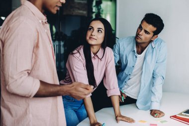 Ofis masasının yanındaki iş birliği sırasında proje fikirleri hakkında iletişim kuran gündelik gömlekli profesyonel hippi erkekler, çok kültürlü erkek ve kadın meslektaşlar detay ve bilgiyi tartışıyor.