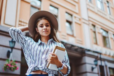 Şık giyinmiş ve şapkalı güzel bir genç kadının yarı boy portresi. Şehir ortamında kameraya bakıyor. Kafkasyalı güzel bir genç kız öğrenci elinde kitap tutuyor ve dışarıda vakit geçiriyor.