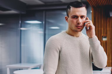 Kendine güvenen genç iş adamının portresi, kameraya bakarken akıllı telefon cihazları ve sorunları çözerken takılıyor. Hücresel alanda konuşan ciddi hippi adam.