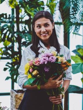 Elinde çiçek açan kompozisyonu olan neşeli Asyalı çiçekçinin yarım boy portresi. Konservatuarda elinde güzel çiçeklerle gülümseyen genç bir botanikçi.