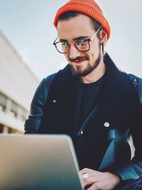 Görme düzeltmesi için optik göz giyimi konusunda başarılı olan erkek serbest yazar dizüstü bilgisayarla proje yaratma konusunda bilgi topluyor, modaya uygun giyinen pozitif hipster adam web sitesinde haber okuyor.