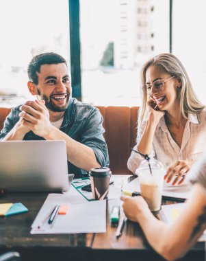 Bir grup neşeli modern kadın ve erkek kafede ders çalışmak ve laptopla bir araya gelip sohbet ederken gülüyorlar.