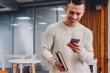 Neşeli genç adam web sitesinde akıllı telefon cihazının komik bildirisini okuyor. 4G internet kullanarak cep telefonundan gülen pozitif hipster öğrenci.