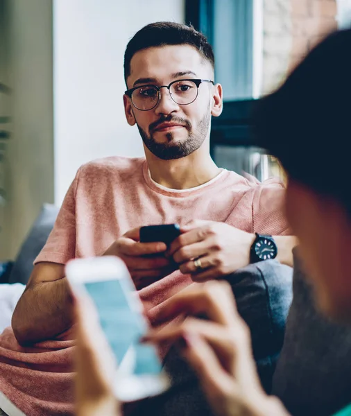Handsome caucasian husband in optical spectacles for provide vision correction looking at millennial wife sitting near and ignoring live communication for chatting online with followers from web page