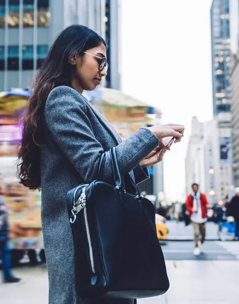 Gözlüklü genç iş kadını New York 'un işlek caddesinden geçerken cep telefonu kullanıyor.