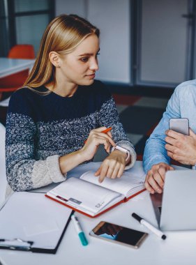 Gündelik kıyafet giyen iki öğrenci dizüstü bilgisayarlarında ders izliyorlar ve modern ofiste not defteriyle birlikte oturuyorlar. Genç adam ve kadının işbirliği ile ortak çalışma projesi hazırlıyorlar.