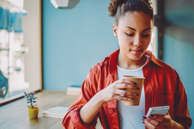 Kafein içeceklerinin tadını çıkarırken akıllı telefon cihazıyla mesaj gönderen çekici, koyu tenli hippi kız, elinde kahve ile elinde kağıt bardak tutan Afrikalı kadın ve web sitesinde politik haberler okuyor.