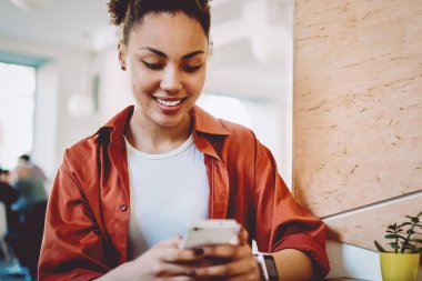 Afro-Amerikalı kadın blogcu mobil iletişim uygulaması üzerinden sohbetten zevk alıyor, pozitif hipster kız cep telefonuyla internete baktığı için komik metinlerle posta yazıyor.