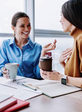 Kafkasyalı neşeli kadın meslektaşlar kahve molası sırasında arkadaşça sohbet ediyorlar. Yaratıcı projeyi birlikte gerçekleştirmekten memnun olan gülümseyen kadın çalışanlar başarılı çalışmaları tartışıyorlar.