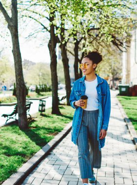 Mutlu bayan turist, tatil sırasında elinde hazır kahveyle yaz caddelerinde gezmekten zevk alıyor. Kot giymiş pozitif hippi kız boş zamanlarında yürüyor.