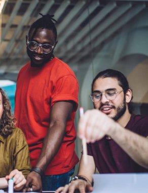 Yaratıcı, etnik çeşitlilikteki kadın ve erkeklerin kağıt posterlere bakıp yeni projeler üzerinde beyin fırtınası yaparken fikir alışverişinde bulunması.