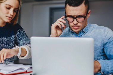 Akıllı genç bir kadın, modern ofisteki masaüstü hipster bir adamla birlikte oturarak, son teslim tarihini ayarlamakla meşgul. Erkek ve kadın tasarımcılar projenin geliştirilmesinde işbirliği yapıyorlar.