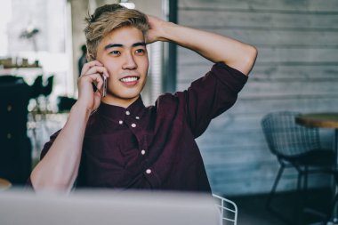 Başarılı genç Asyalı iş adamı, modern uzayda dizüstü bilgisayarın uzaktan kumandası sırasında operatörle birlikte akıllı telefondan arıyor. Çinli hippi adam cep telefonuyla eğleniyor.