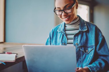 Pozitif esmer tenli kız öğrenci boş zamanlarında online alışveriş yapıyor, optik gözlüklü mutlu genç internet sitelerinde popüler internet sitelerinde komik videolar izliyor.