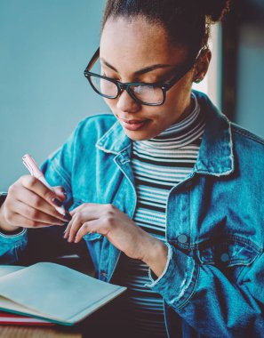 Zarif kot giyimli çekici bir kız öğrenci bilgi kitaplarından bilgi okuyor ve ders çalışma planını analiz ediyor, koyu tenli hippi kız öğreniyor ve üniversite sınavlarına hazırlanıyor.