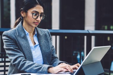 Zarif kıyafetli ve gözlüklü zeki iş kadını New York şehrinin terasındaki tablete e-posta gönderen bir belgeyle masada oturuyor.