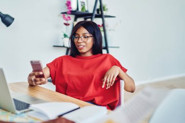 Gülümseyen Afro-Amerikan kadın blog yazarı cep telefonundan sosyal ağlardan gelen uyarıları kontrol ediyor, akıllı telefondan mesaj okuyan ve netbook ile çalışan bir kadın öğrenci görüntüsü.