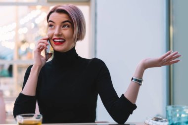 Siyah giysili ve kol saati takmış neşeli, genç ve şaşkın bir kadın boş tabletle masada oturuyor ve bir fincan yeşil çayla kafede telefon edip gözlerini kaçırıyor.