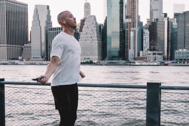 Genç, kısa saçlı, kulaklıkla müzik dinleyen, metal tel örgülerin yanında ip atlayan etnik bir adamın yan görüntüsü.