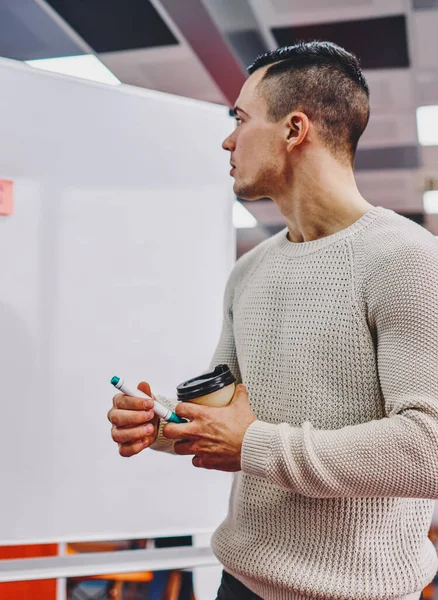 Concentrated young man working coach and looking at flip chat with stickers during productive business workshop.Pensive hipster student dressed in casual wear checking written information on board