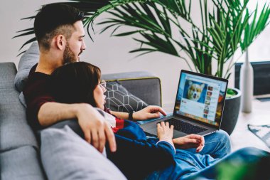 Genç bir adam ve bir kadın, rahat oturma odasında rahat bir kanepe, ilişki ve iletişim konsepti üzerinde dinlenirken ücretsiz ev Wi-Fi 'sine bağlı sosyal ağda sohbet etmek için internette geziniyorlar.