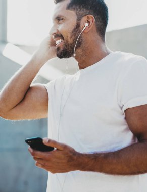 Boş tişörtlü, mutlu ve mutlu bir adamın bakışları. Motivasyon konsepti olan sesli kitapları dinlerken gülümsemesi. Elektronik kulaklıklı neşeli bir erkek.